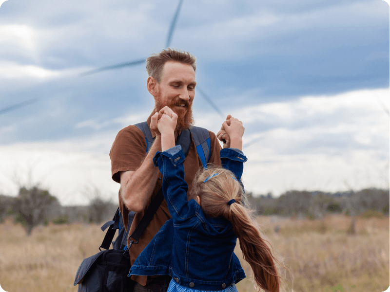 father and daughter holding hands with wind turbines in the background