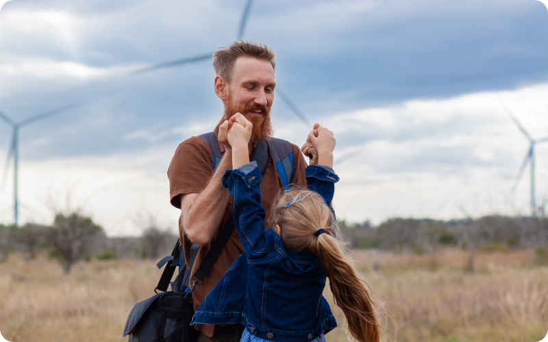 father and daughter holding hands with wind turbines in the background