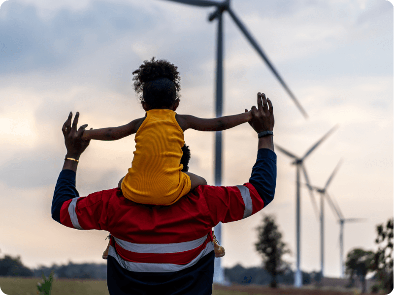 Girl on her dads shoulders with wind turbines in background