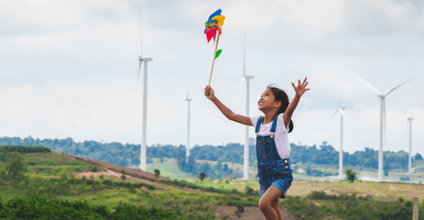 young girl playing with wind turbines behind her