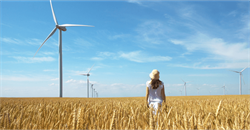 Woman stood in wheat field with wind turbines in background